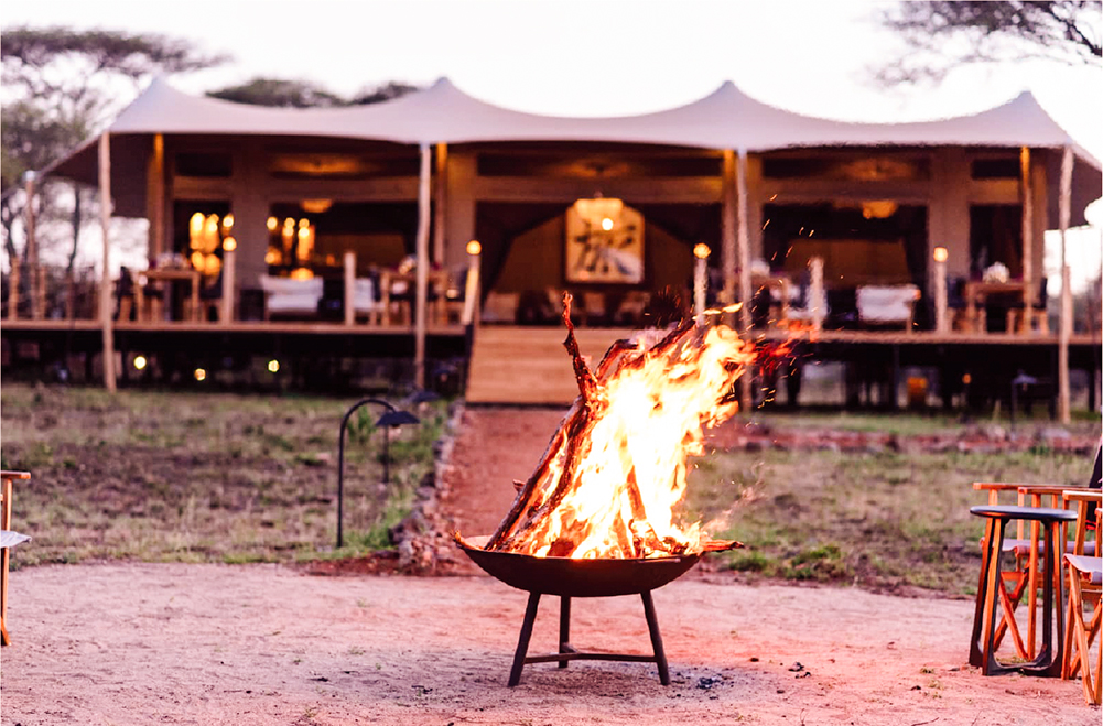 Campfire in front of luxury safari tent at Tabi Camp in Serengeti during evening